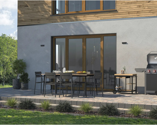 Terrasse avec table à manger, chaises, barbecue et chariot de barbecue devant une maison