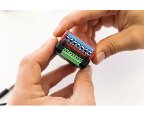 Hände halten ein elektronisches Bauteil mit Anschlussklemmen