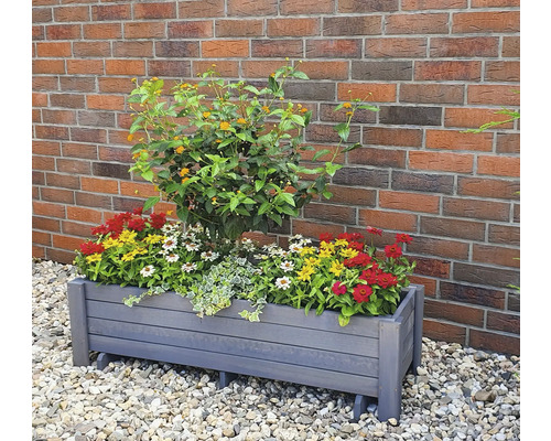 Jardinière en bois avec des fleurs colorées et une plante devant un mur de briques
