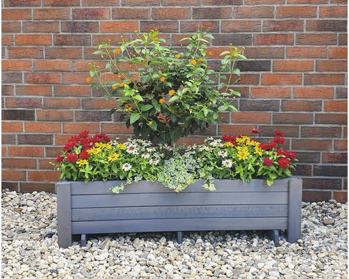 Jardinière rectangulaire en bois plantée de diverses fleurs devant un mur de briques