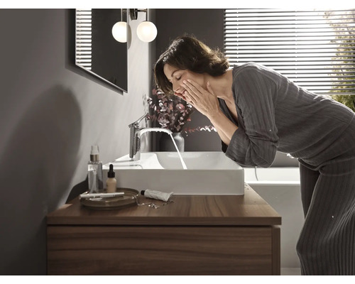 Frau wäscht sich das Gesicht an einem rechteckigen Waschbecken mit Armatur auf einem Holzunterschrank