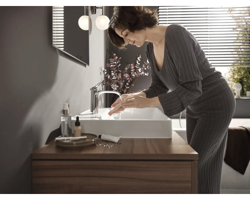 Badezimmer mit Waschtisch, Armatur, Spiegel und Frau beim Händewaschen