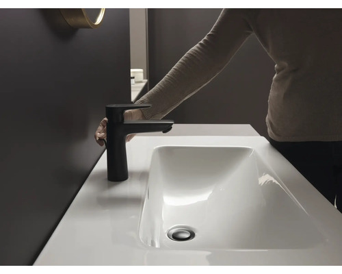 Person bedient einen schwarzen Wasserhahn an einem Waschbecken