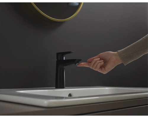 Waschbeckenarmatur in einem Badezimmer mit einer Hand, die den Knopf berührt.