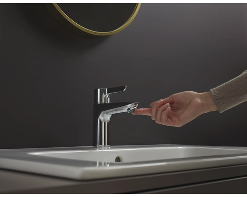 Eine Hand betätigt einen Wasserhahn aus Metall auf einem Waschbecken.