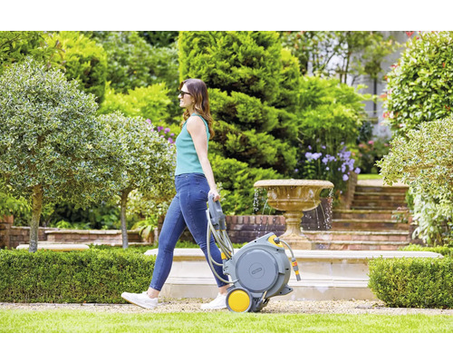 Femme tirant un chariot de tuyau d''arrosage dans un jardin avec fontaine.