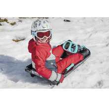 Ein Kind mit Helm und Skibrille sitzt auf einem Schlitten im Schnee.