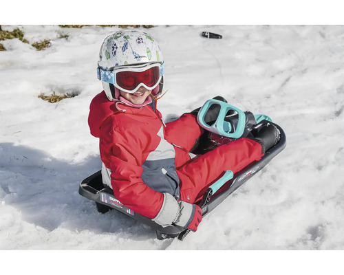 Un enfant avec un casque et des lunettes de ski est assis sur une luge dans la neige.