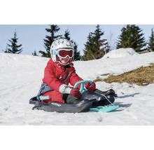 Kind mit Helm und Skibrille auf einem Rodelschlitten im Schnee.