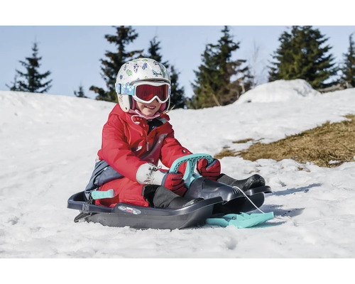 Enfant avec casque et lunettes de ski sur une luge dans la neige.