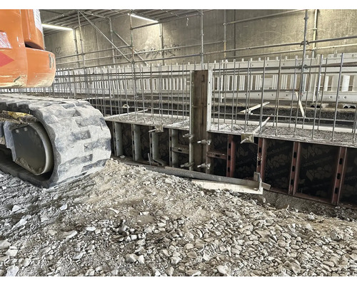 Fouille avec coffrage et fers d''armature, pelle sur chenilles au premier plan.