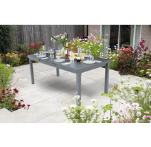 Table de jardin grise extensible avec vaisselle et fleurs dans le jardin