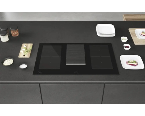 Plaque à induction noire Haier avec hotte aspirante dans un comptoir de cuisine.