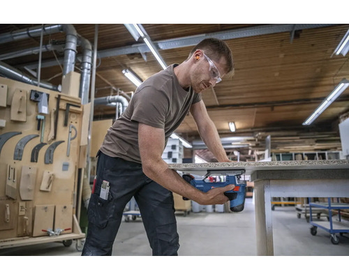 Un homme sciant une pièce à travailler avec une scie sauteuse dans un atelier.