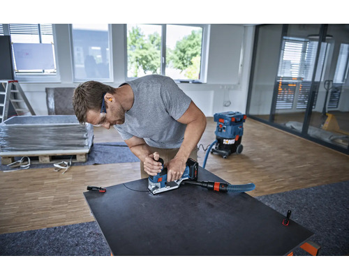 Un homme utilise une ponceuse avec aspirateur sur une plaque sombre dans une pièce lumineuse.