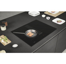Plaque à induction noire Haier avec hotte intégrée dans un plan de travail de cuisine avec une poêle contenant du saumon.