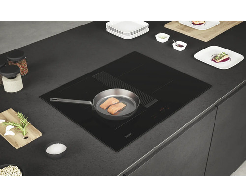 Plaque à induction noire Haier avec hotte intégrée dans un plan de travail de cuisine avec une poêle contenant du saumon.