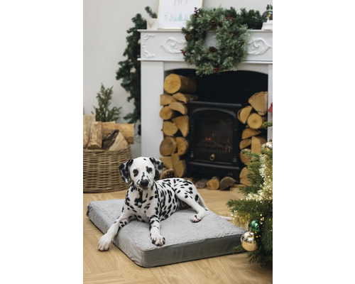 Dalmatien allongé sur un lit pour chien gris devant une cheminée et un sapin de Noël.