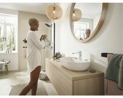 Helles Badezimmer mit Waschtisch, Spiegel, Deckenleuchten und einer Frau, die sich abtrocknet