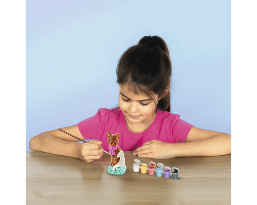 Une fille peint une sculpture de chat avec des pinceaux et des peintures.