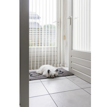 Chien allongé sur un paillasson en forme d''os devant une porte de patio avec grille de sécurité