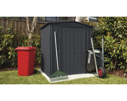 Gartenszene mit Gerätehaus, Mülltonne, Schubkarre und Rechen im Aussenbereich.