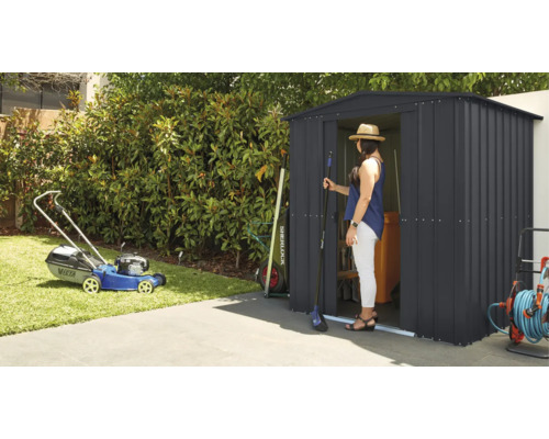 Gartenszene mit Rasenmäher und Geräteschuppen, in dem eine Frau steht