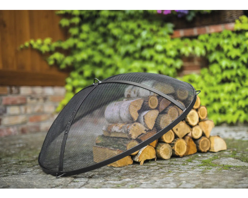 Schwarzer Funkenschutz aus Metall mit Holzscheiten im Garten.