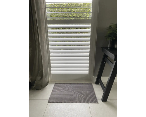 Innenaufnahme eines grauen Fußabstreifers mit geometrischem Muster vor einer weißen Jalousie