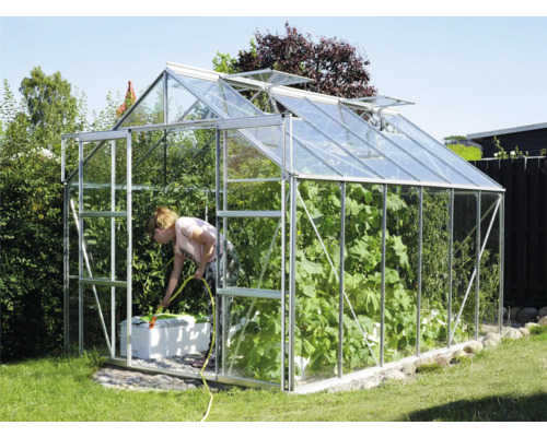 Gewächshaus im Garten mit Frau beim Bewässern der Pflanzen