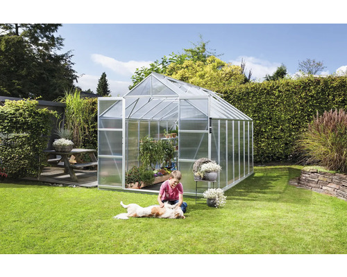 Gewächshaus im Garten mit spielendem Kind und Hund auf dem Rasen.