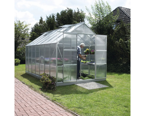 Gewächshaus mit Person, Pflanzen und Regalen im Garten.