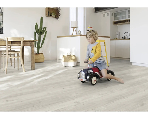 Heller Wohnraum mit Holztisch, Kaktus, Junge auf Spielzeugauto und hellem Holzboden.