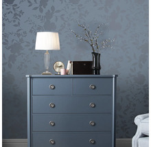 Kommode mit Lampe, Uhr und Dekoration vor floral gemusterter Wand