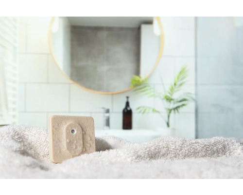 Quadratischer, beiger Duschabzieher auf einem Handtuch in einem Badezimmer.