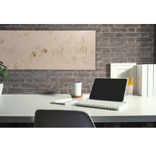 Schreibtisch mit Tablet, Tastatur, Tasse und Dekorationspaneel vor einer Backsteinwand