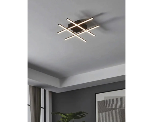 Moderne Deckenleuchte mit sich kreuzenden LED-Leuchtstäben in einem Wohnzimmer.