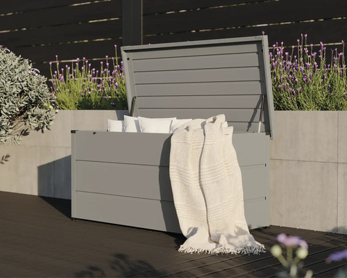 Geöffnete, graue Gartenbox mit Kissen und einer Decke auf einer Terrasse