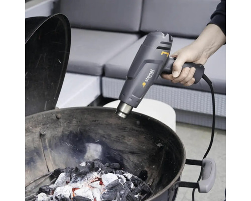 Une personne allume du charbon de bois avec un décapeur thermique Steinel.