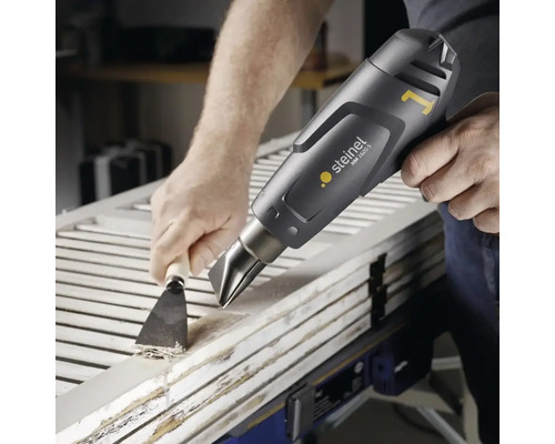 Artisan en train d''enlever de la peinture sur une porte en bois avec un décapeur thermique et un grattoir