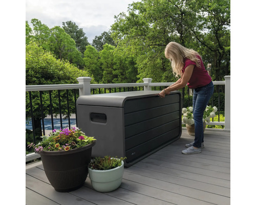 Frau öffnet eine wetterfeste Aufbewahrungsbox auf einer Terrasse.