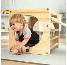 Un enfant grimpe dans un cube de jeu en bois avec des barreaux et un toboggan dans une chambre d''enfant.