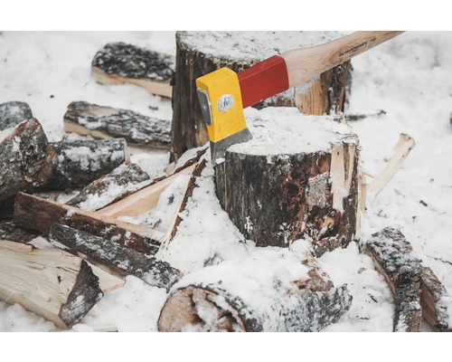 Axt steckt im Holzstamm mit Holzstücken im Schnee