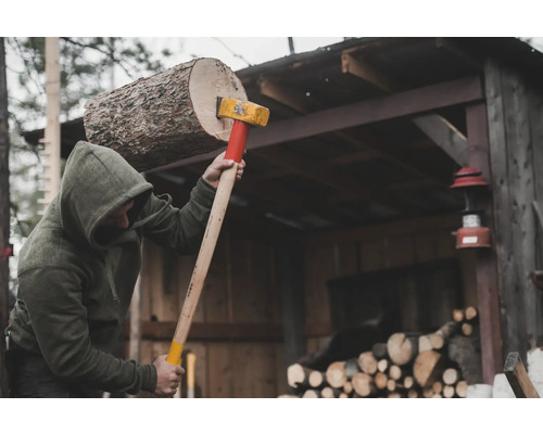 Personne fendant du bois avec une hache devant un hangar à bois.