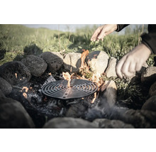 Feuerstelle mit Grillrost, umrandet von Steinen, mit Händen darüber