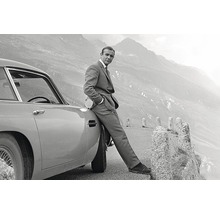 Sean Connery appuyé sur une Aston Martin devant un paysage de montagne.
