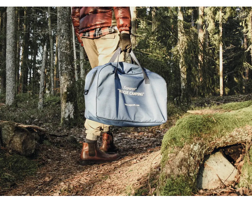 Person trägt blaue Campingtoilette in einer Tragetasche im Wald