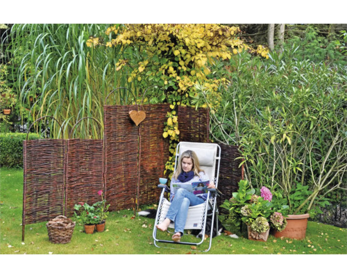 Gartenszene mit Weiden Sichtschutz, Liegestuhl und bepflanzten Blumentöpfen auf einer Rasenfläche