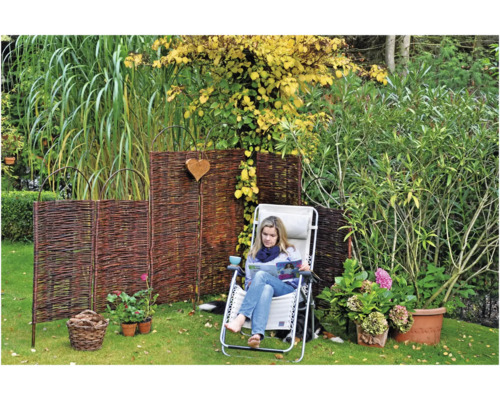 Scène de jardin avec clôture en osier, chaise longue et femme lisant dans le jardin