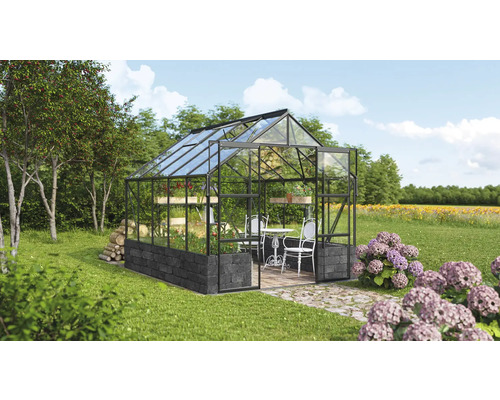 Serre avec murs en verre, base en pierre et coin salon dans le jardin